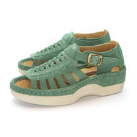 A pair of women's open-toe sandals in a mint suede, featuring cutout straps, a braided front design, adjustable ankle straps with silver buckles, and white soles.