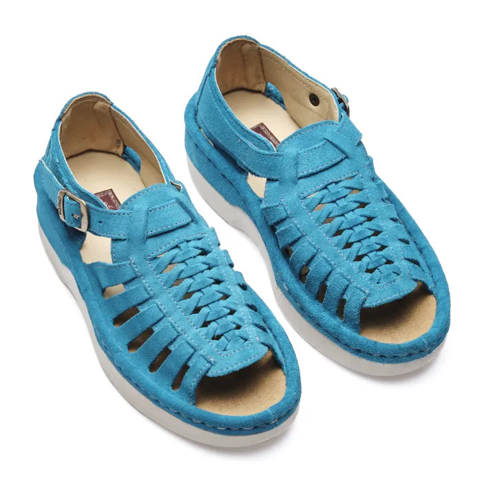 A pair of women's open-toe sandals in a vibrant turquoise blue suede, featuring cutout straps, a braided front design, adjustable ankle straps with silver buckles, and white soles.