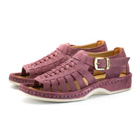 A pair of strappy sandals in lilac suede, featuring a cutout design, braided detail across the front, an adjustable ankle strap with a gold-tone buckle, and a low wedge heel. The brand 'Omega' is visible on the buckle.