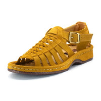 A single strappy sandal in mustard yellow suede, featuring a buckle strap, braided front straps, and a wedge sole, shown against a plain white background.