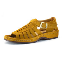 A single strappy sandal in mustard yellow suede, featuring a buckle strap, braided front straps, and a wedge sole, shown against a plain white background.