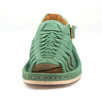 A mint green suede wedge sandal with a multi-cut strap design, a gold buckle, and a white sole, shown in a side profile on a white background.