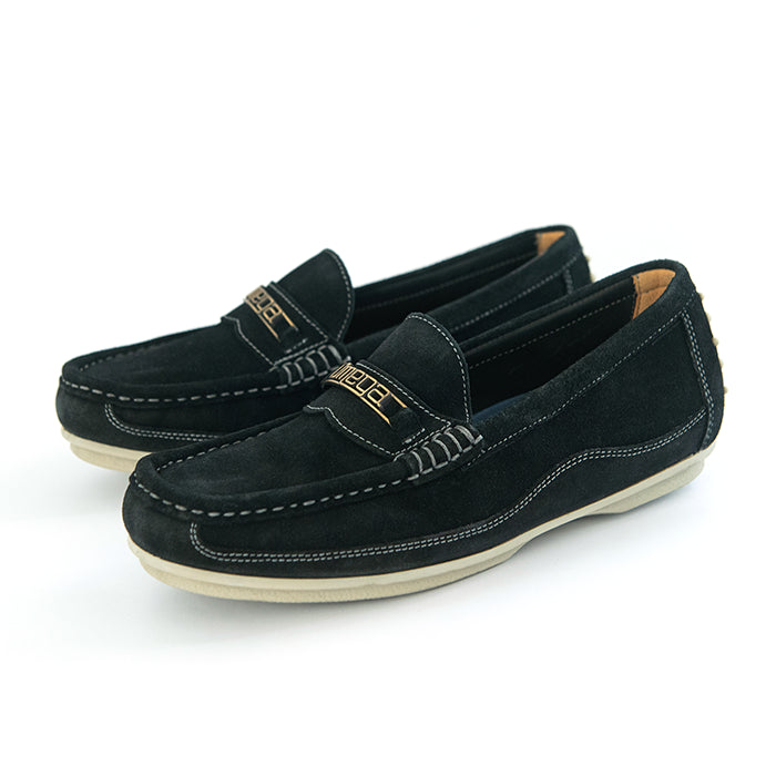 A pair of black suede penny loafers with gold lettering on the strap, white contrast stitching, and off-white soles, shown on a white background.